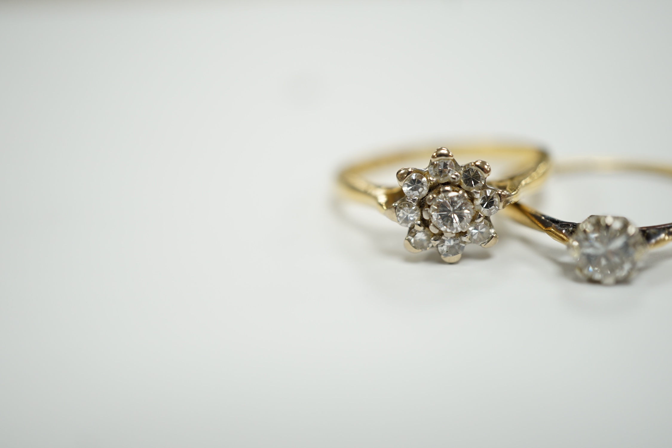 An 18ct gold and diamond cluster set flower head cluster ring, size K and an 18ct, plat. and solitaire diamond set ring, size L, gross weight 4.3 grams.